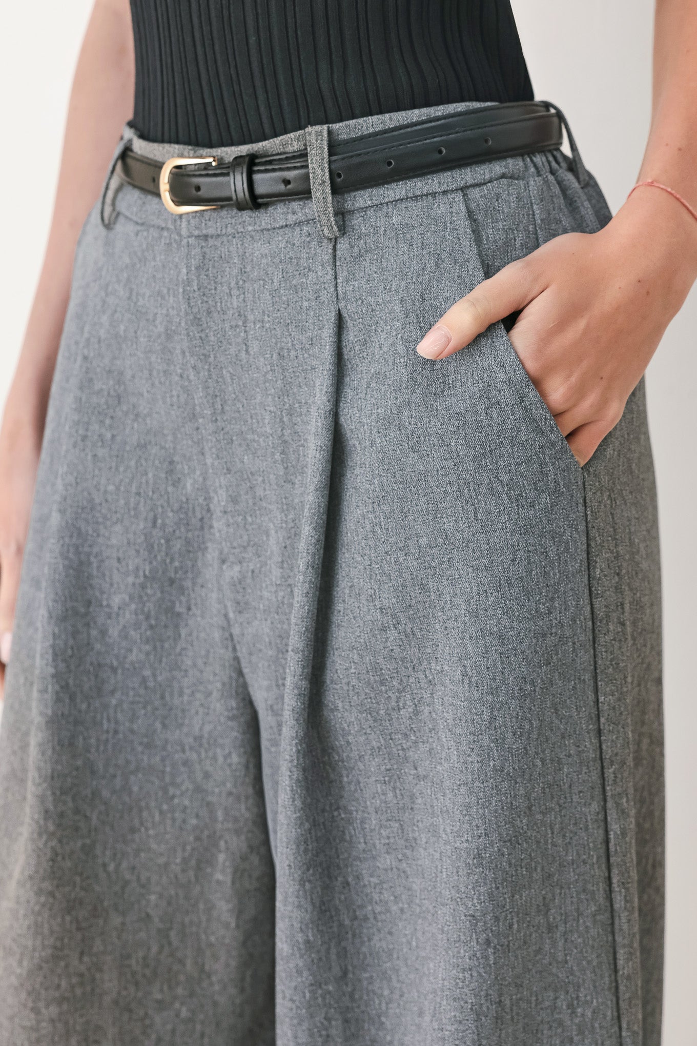 Woman wearing gray wide-leg pant with front closure, single pleat, pockets, and black belt | FREEMARKET