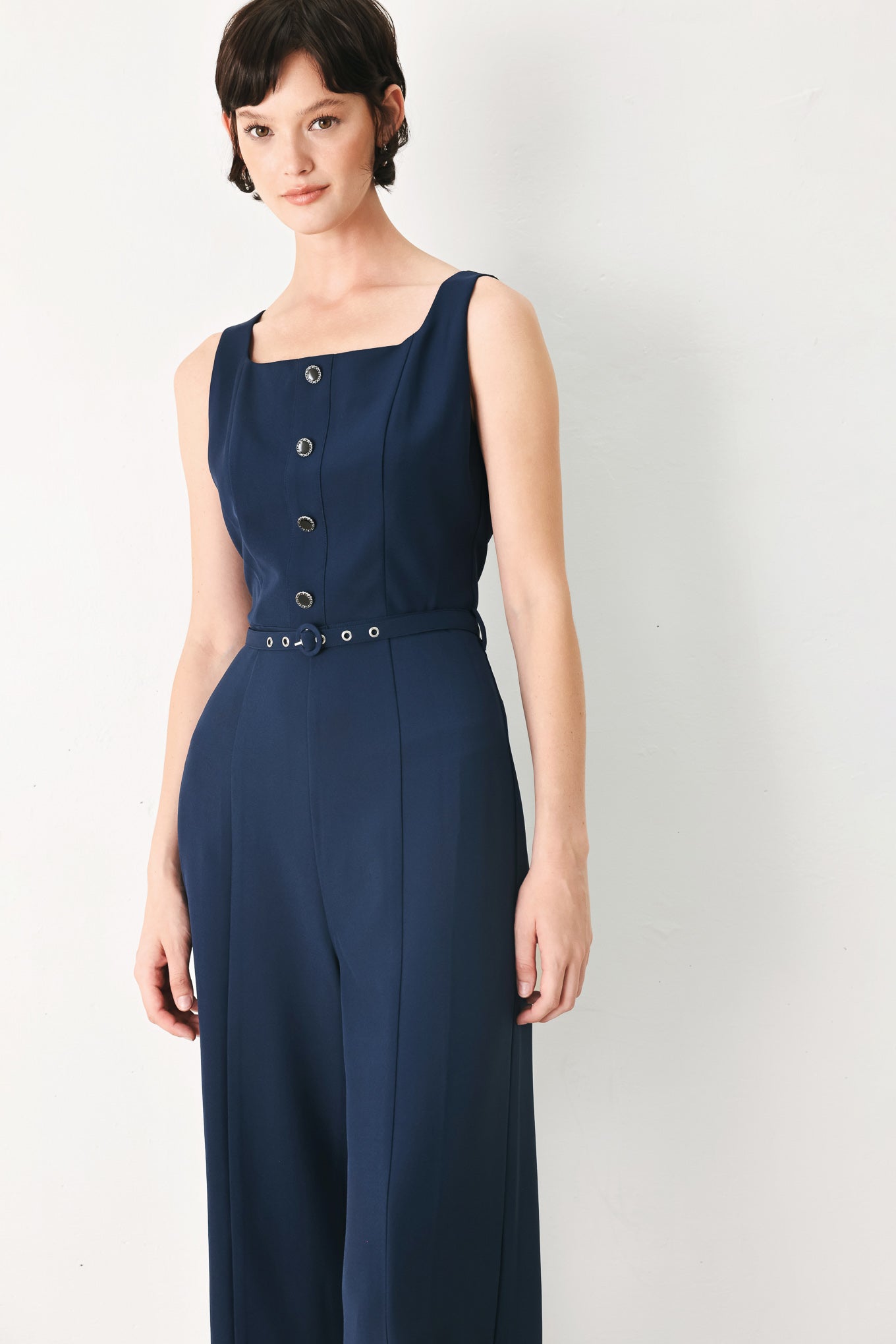 Woman wearing a sleeveless navy blue jumpsuit featuring square neckline, front button detail, self belt, wide leg and back zipper closure | FREEMARKET