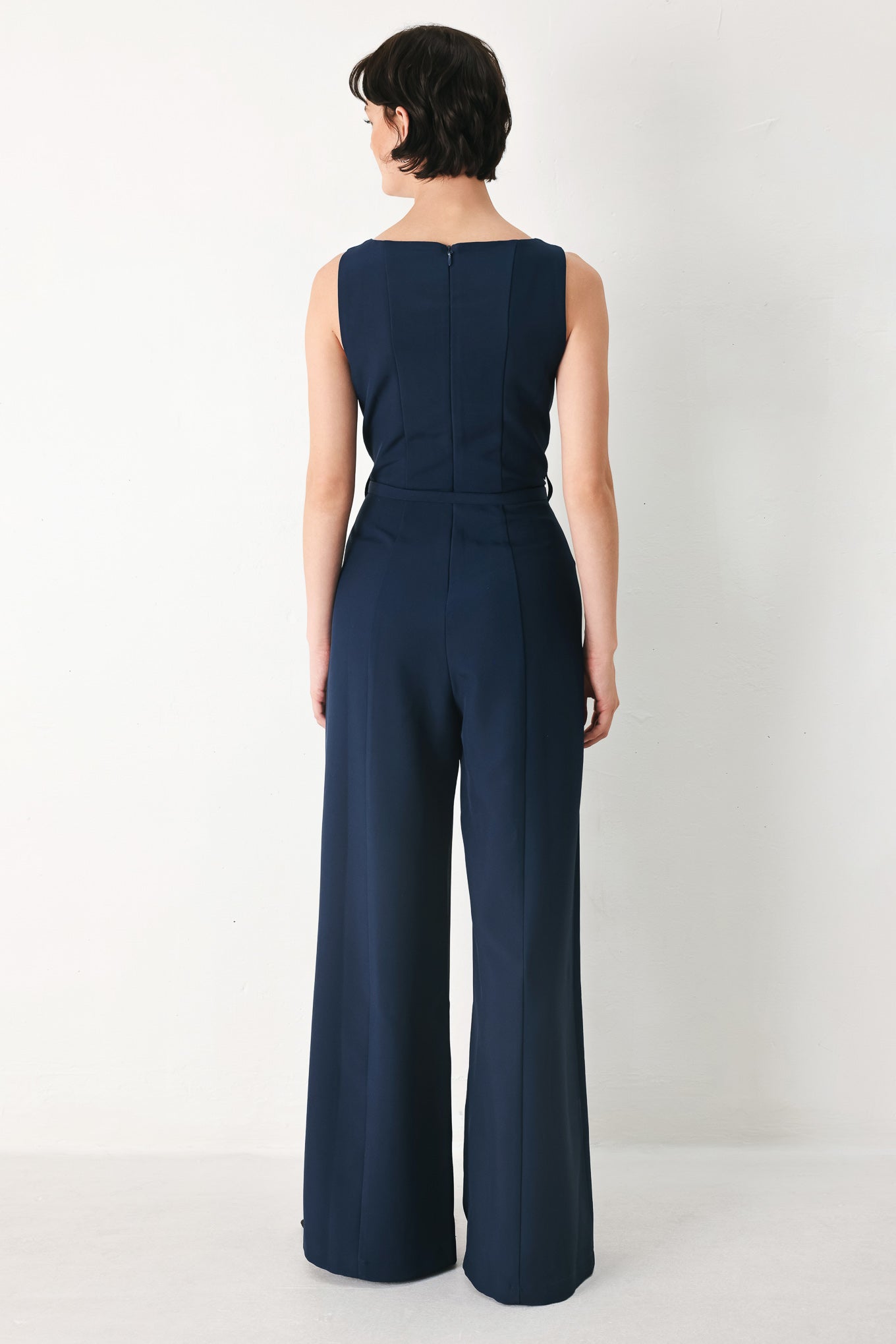 Woman wearing a sleeveless navy blue jumpsuit featuring square neckline, front button detail, self belt, wide leg and back zipper closure | FREEMARKET