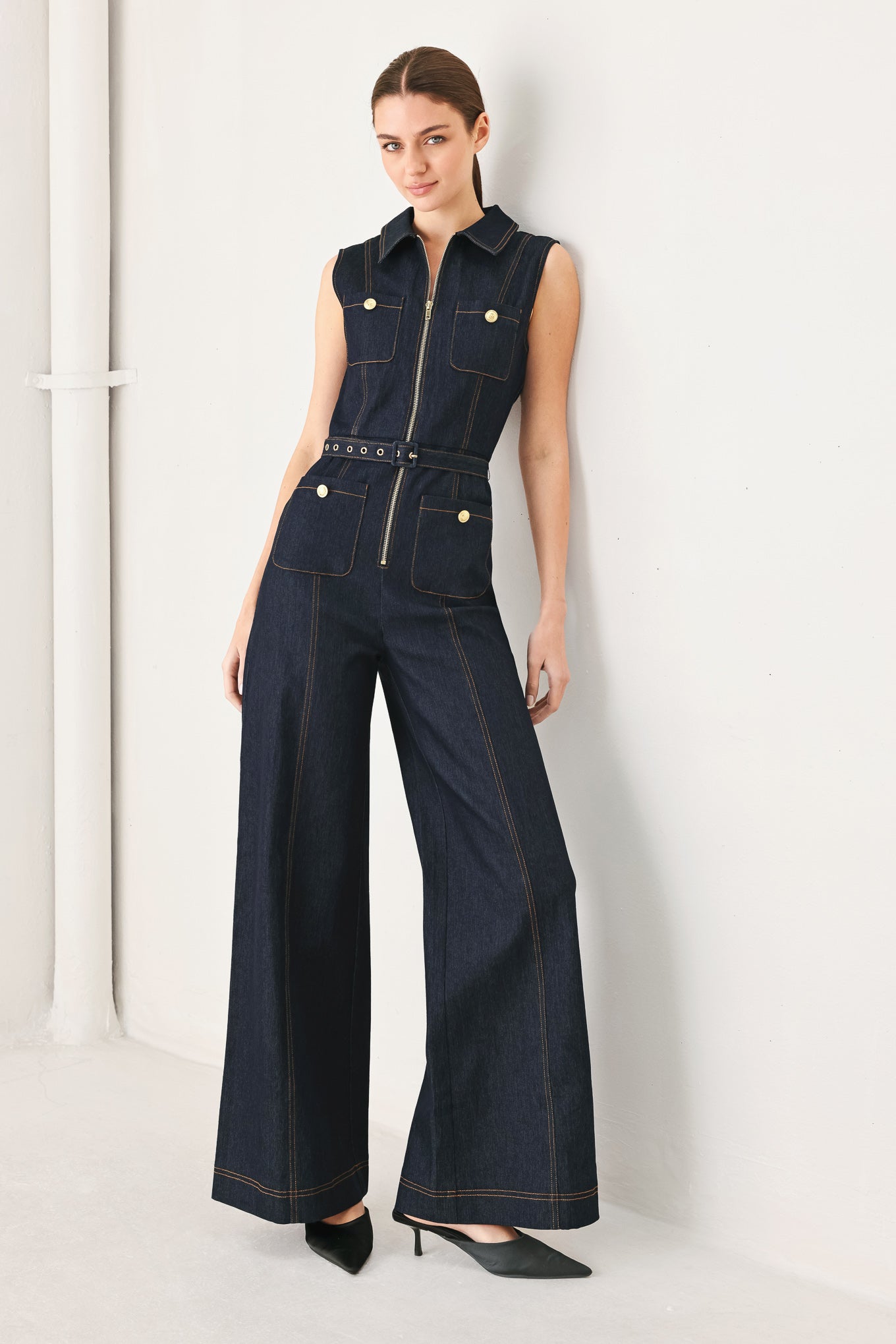 A denim jumpsuit featuring collar, sleeveless, front zipper closure, pockets and wide leg