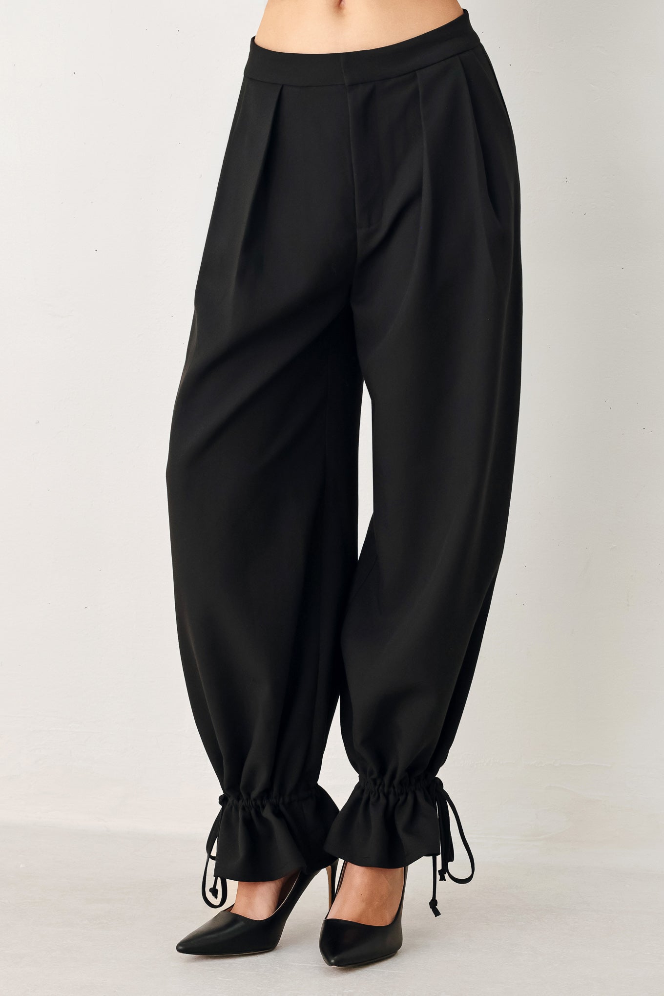 Black harem pants with drawstring ankles on a plain background