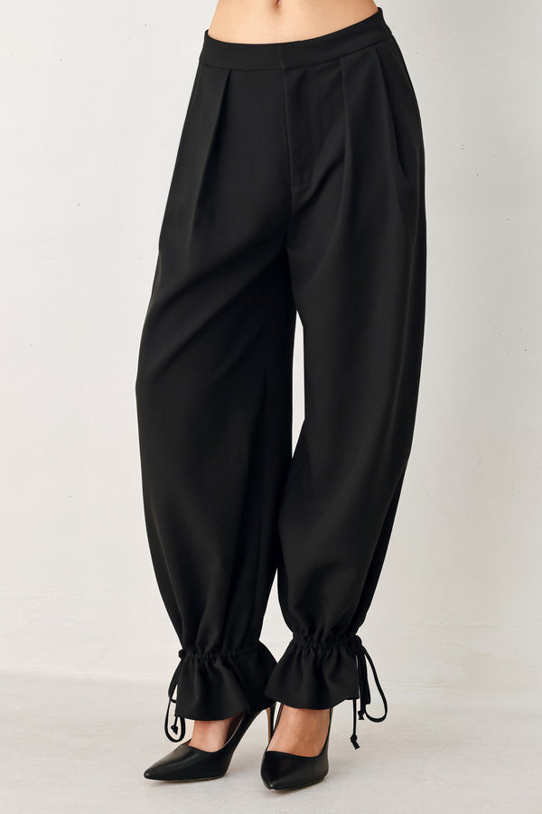 Woman wearing black harem pants with drawstring ankles and front pleats | FREEMARKET