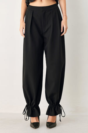 Woman wearing black harem pants with drawstring ankles and front pleats | FREEMARKET