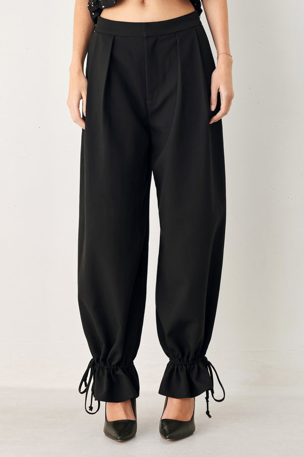 Woman wearing black harem pants with drawstring ankles and front pleats | FREEMARKET
