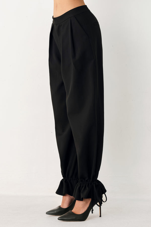 Woman wearing black harem pants with drawstring ankles and front pleats | FREEMARKET
