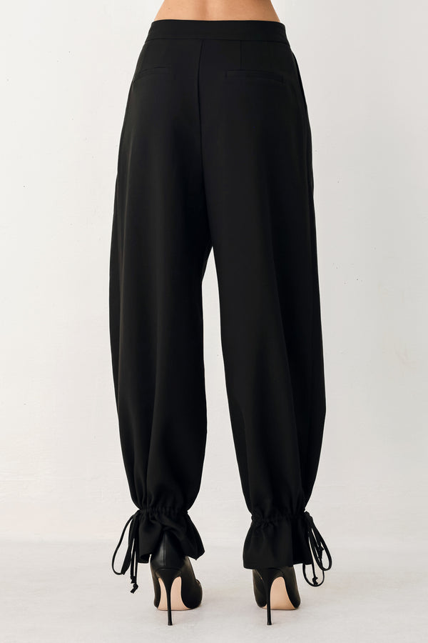 Woman wearing black harem pants with drawstring ankles and front pleats | FREEMARKET
