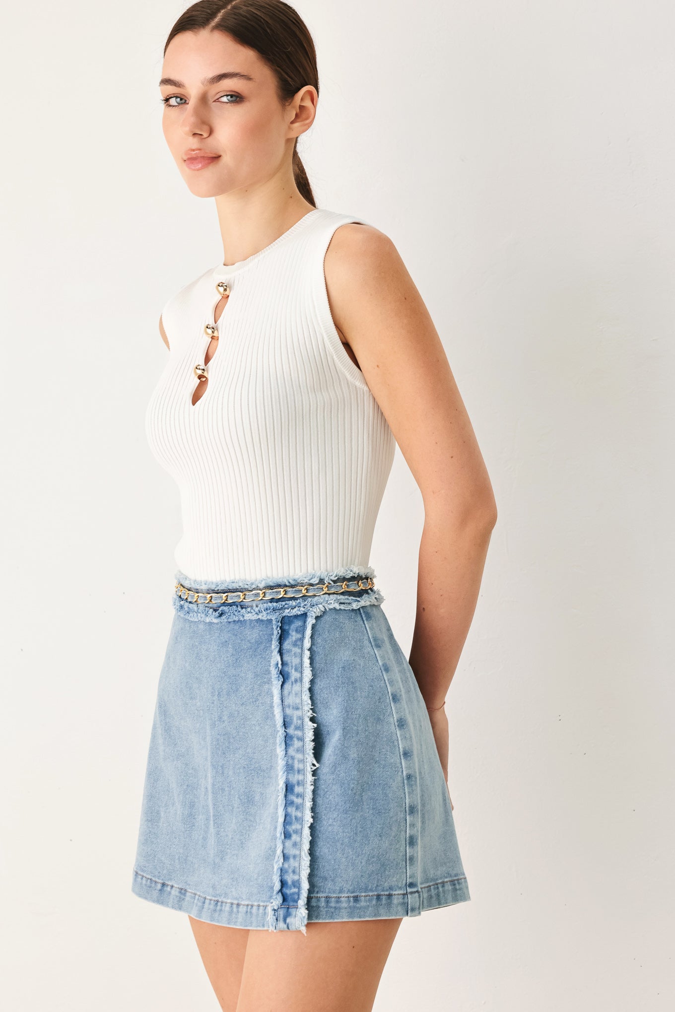 Woman wearing a light denim skort with fray edge, chain waist detail and back zipper closure | FREEMARKET