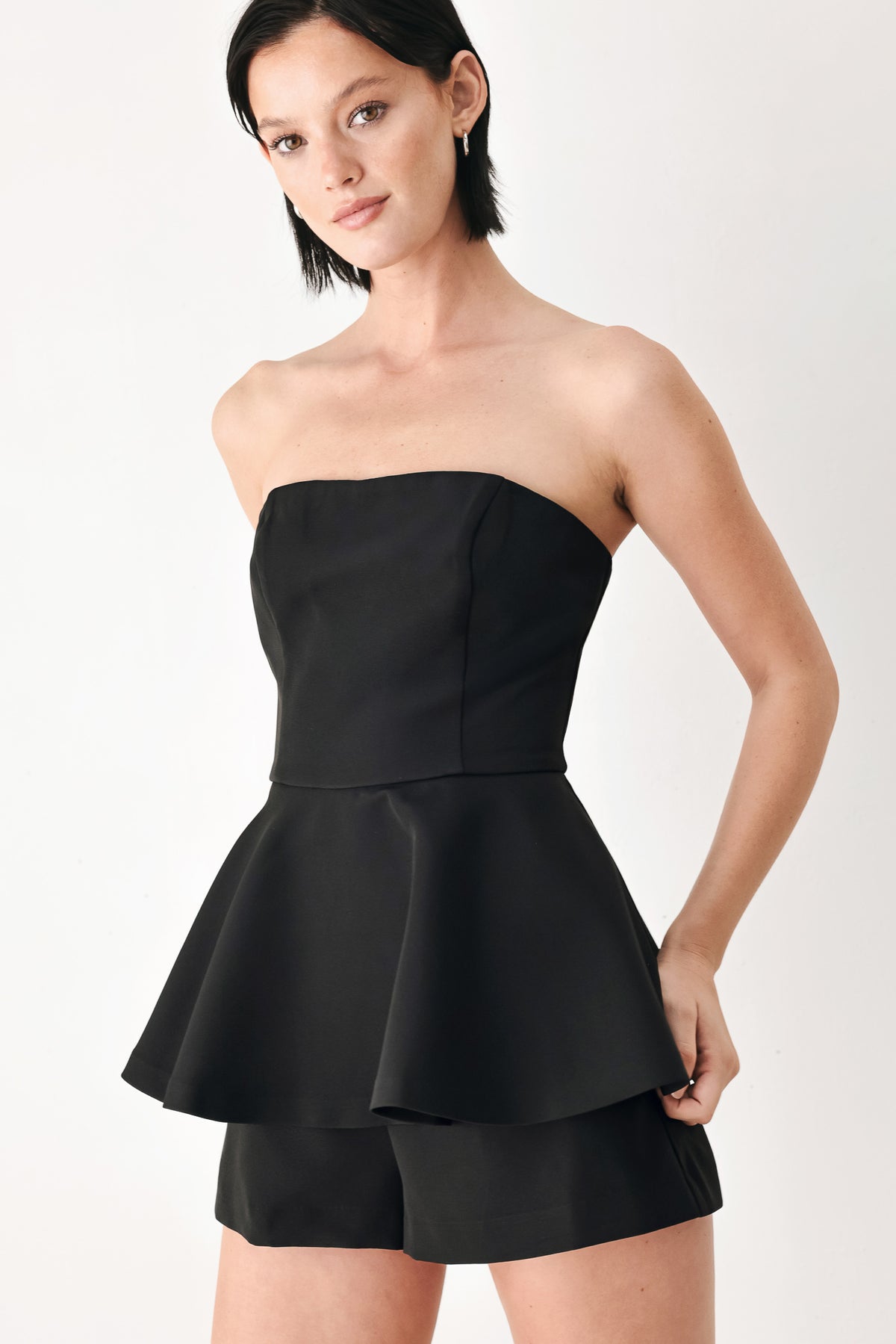 A woman modeling a black strapless peplum romper | FREEMARKET