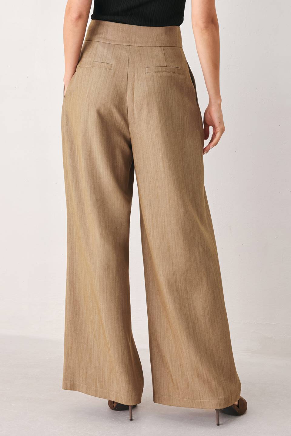 A model wearing high-waisted, wide-leg trousers in a light tan color with buttons | FREEMARKET