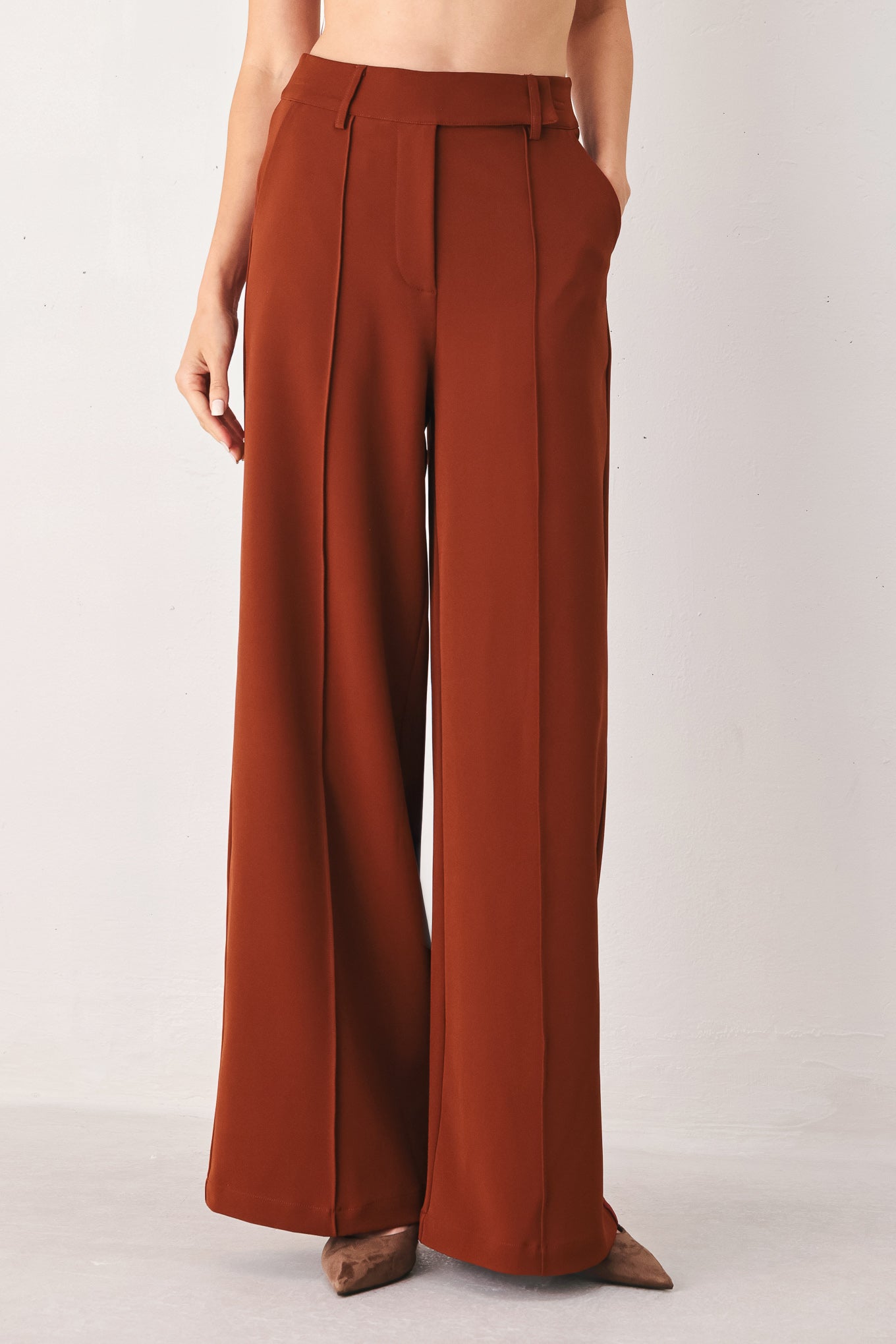 A woman wearing a pair of high-waisted, wide-leg trousers in a warm rust brown color | FREEMARKET