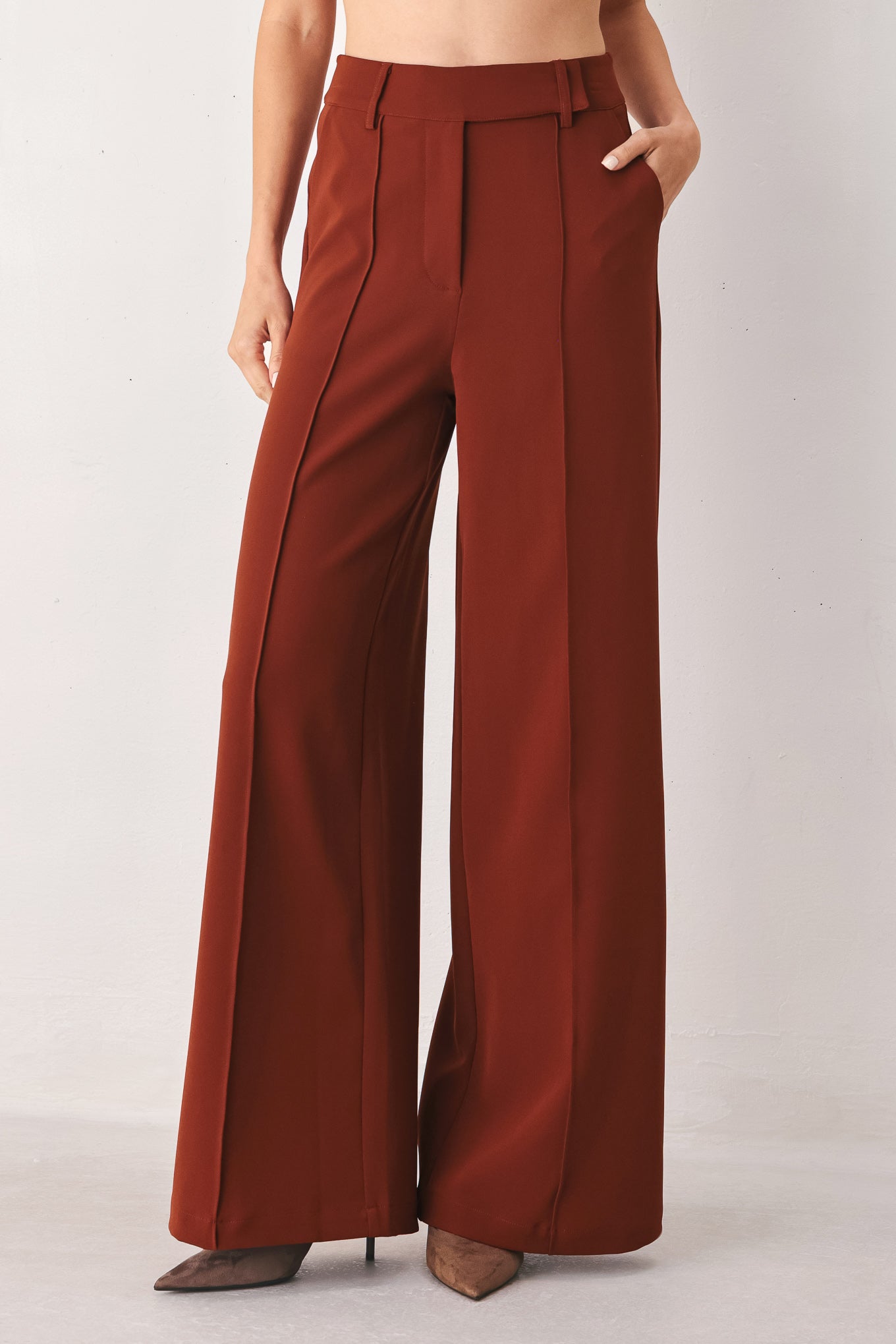 A woman wearing a pair of high-waisted, wide-leg trousers in a warm rust brown color | FREEMARKET
