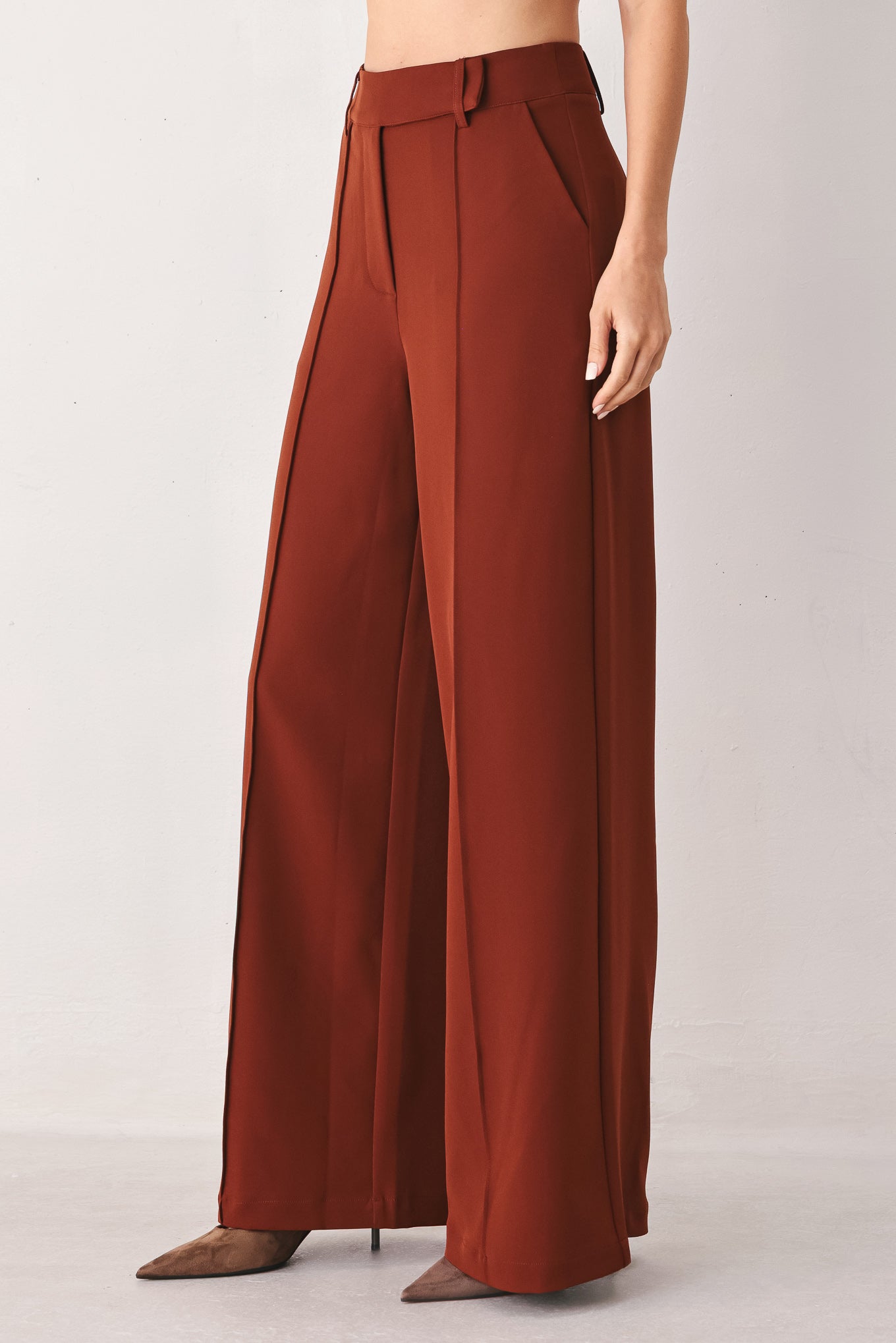 A woman wearing a pair of high-waisted, wide-leg trousers in a warm rust brown color | FREEMARKET
