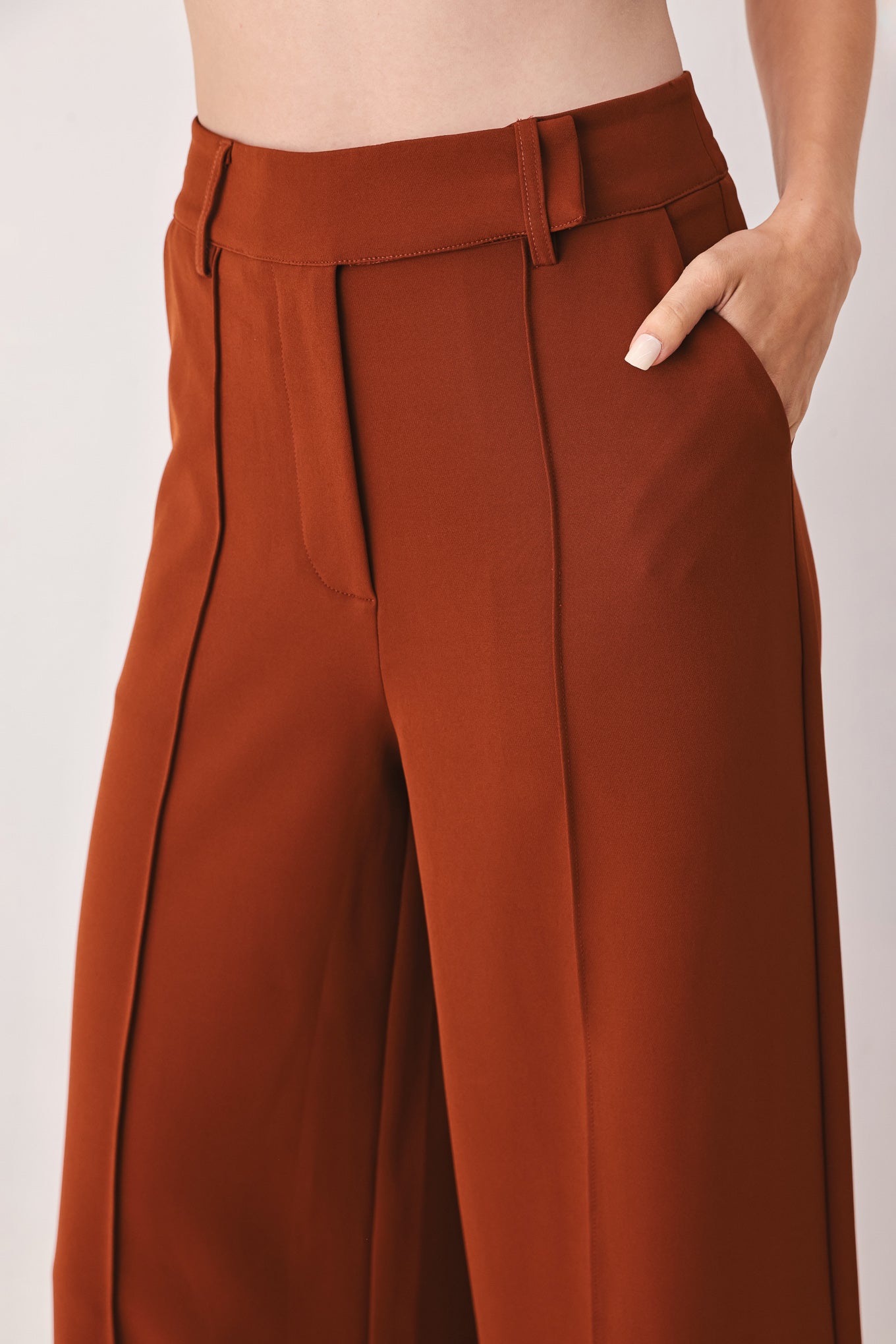 A woman wearing a pair of high-waisted, wide-leg trousers in a warm rust brown color | FREEMARKET
