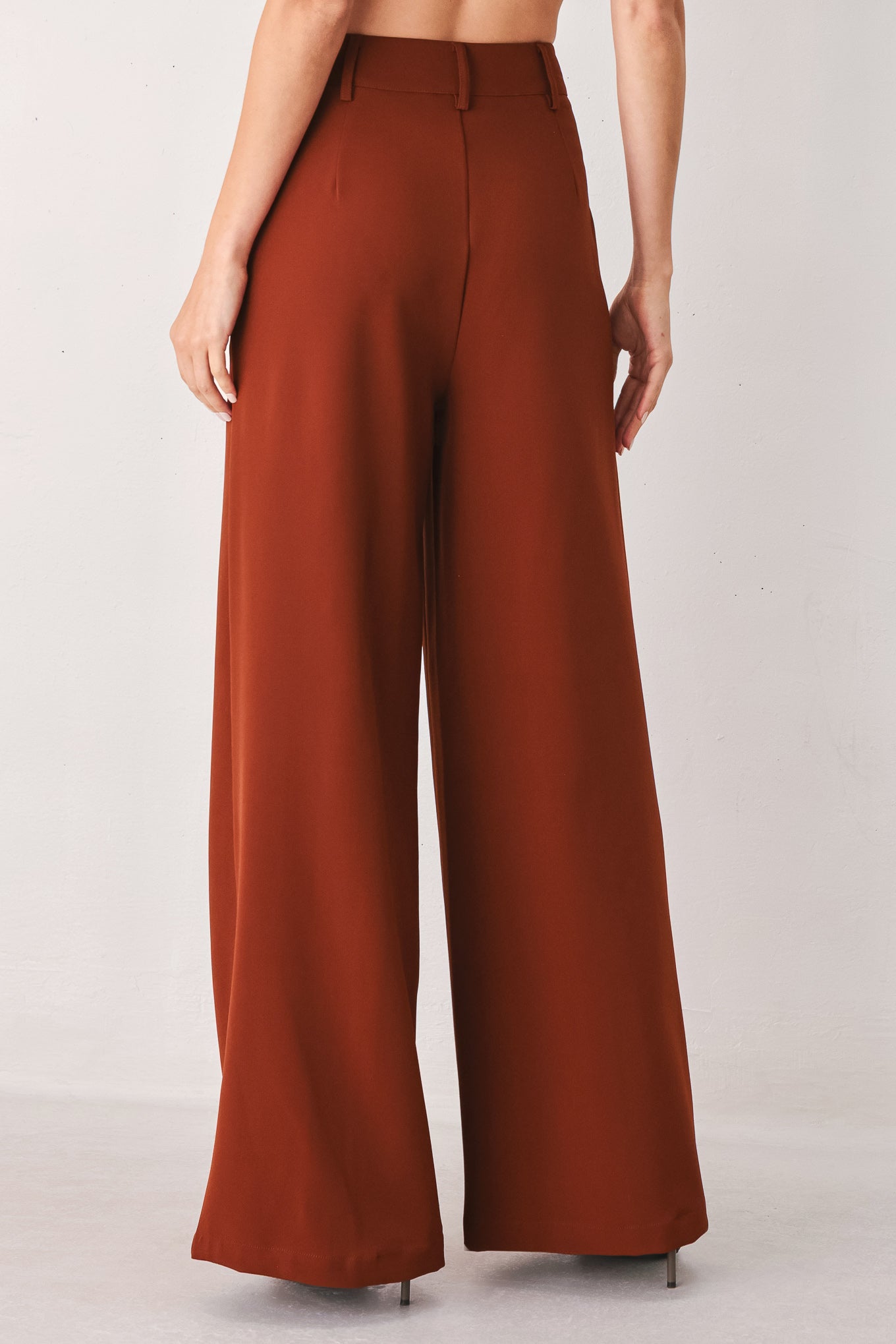 A woman wearing a pair of high-waisted, wide-leg trousers in a warm rust brown color | FREEMARKET