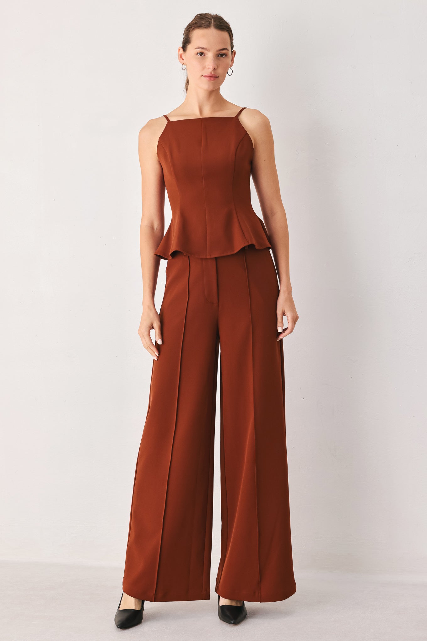 A woman wearing a pair of high-waisted, wide-leg trousers in a warm rust brown color | FREEMARKET