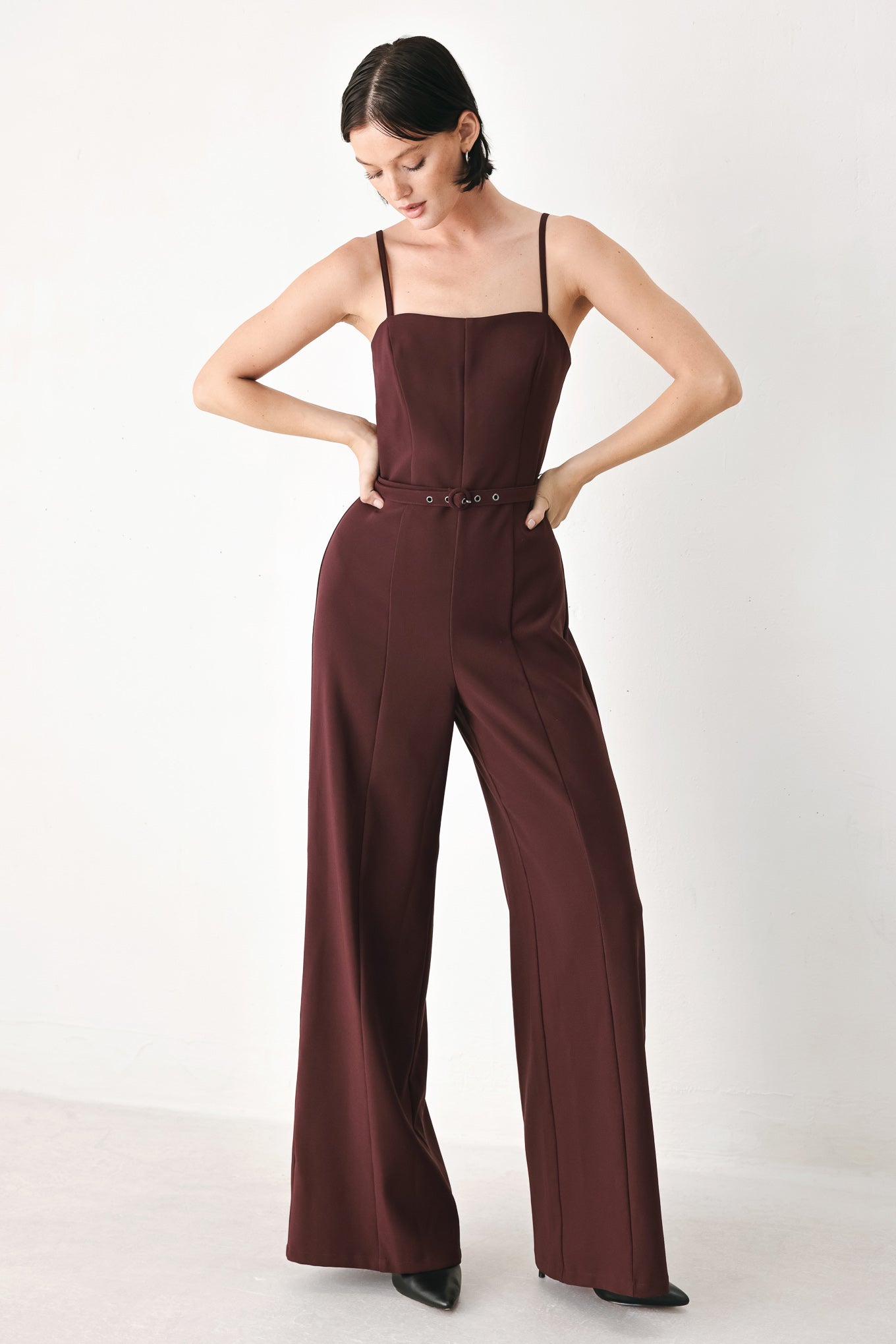 A woman modeling a dark burgundy wide-leg jumpsuit with thin spaghetti straps and a matching waist belt | FREEMARKET