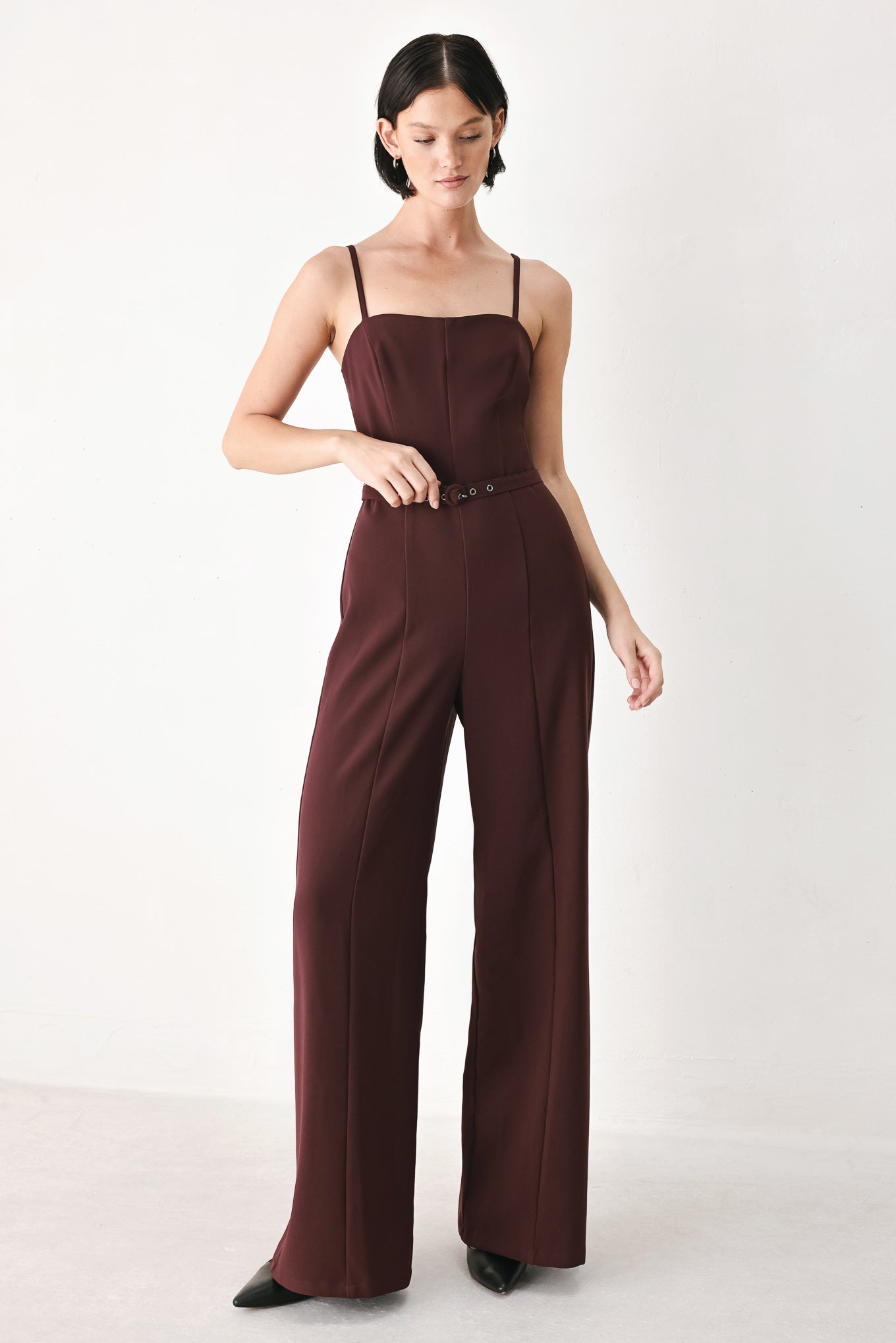 A woman modeling a dark burgundy wide-leg jumpsuit with thin spaghetti straps and a matching waist belt | FREEMARKET