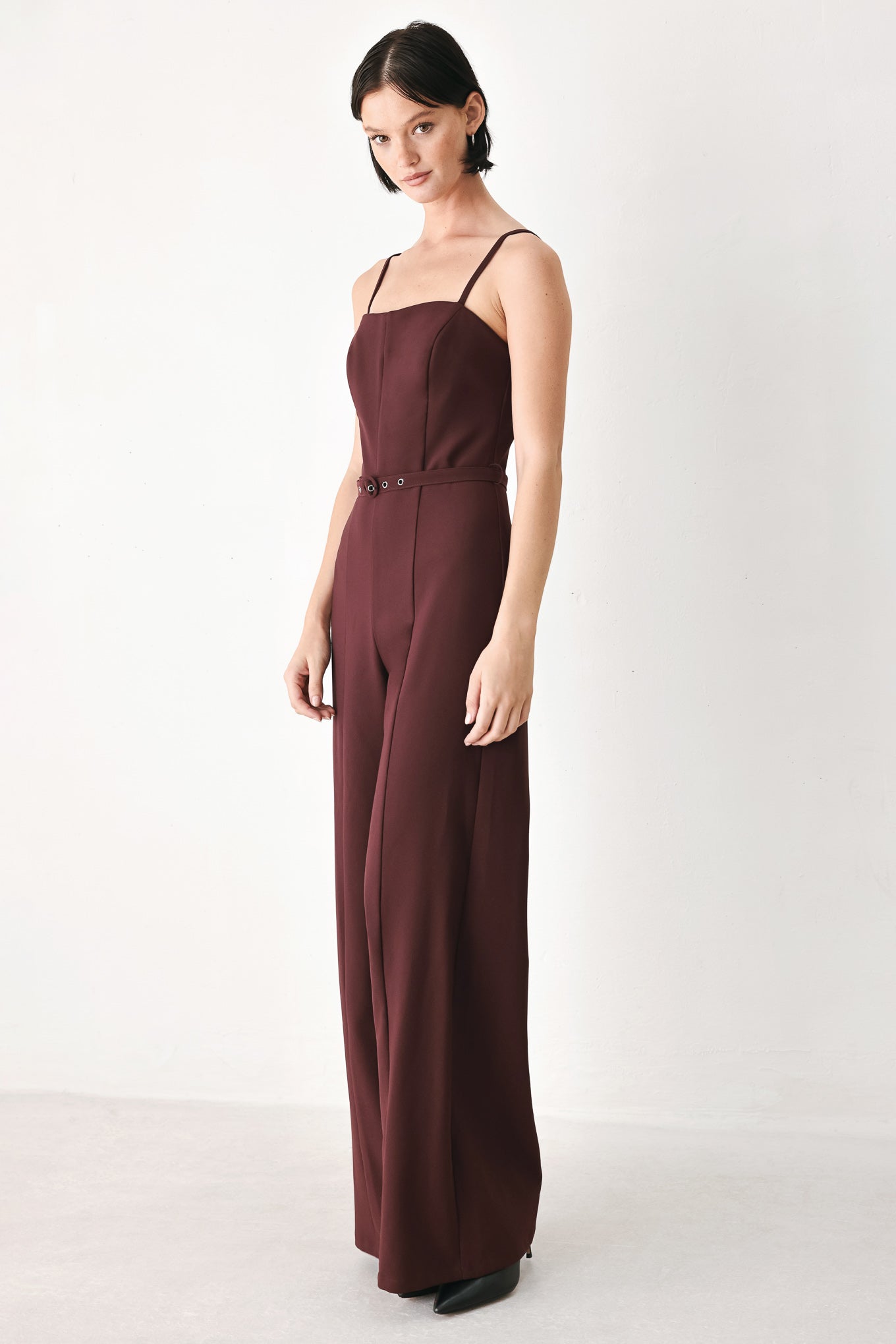 A woman modeling a dark burgundy wide-leg jumpsuit with thin spaghetti straps and a matching waist belt | FREEMARKET