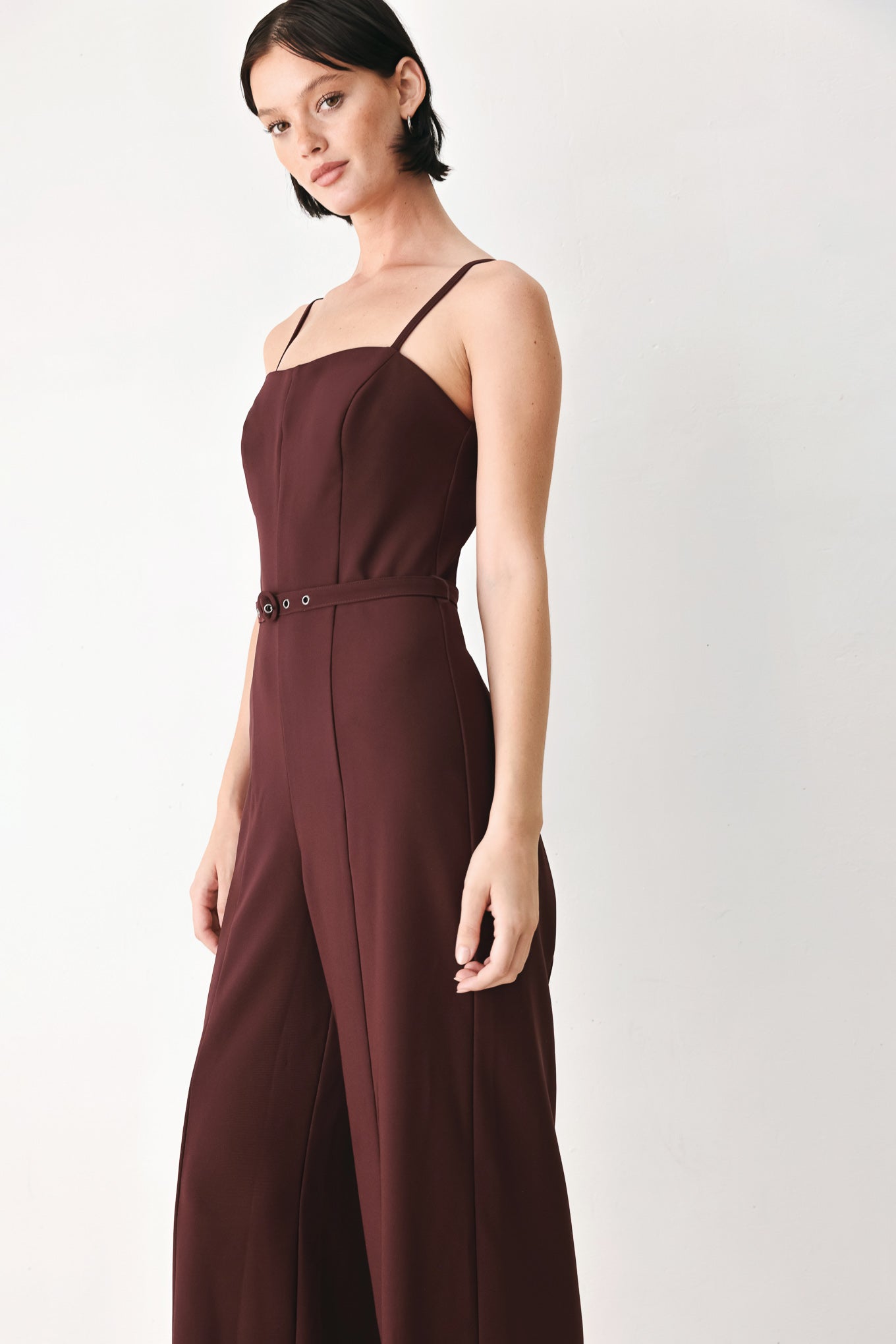 A woman modeling a dark burgundy wide-leg jumpsuit with thin spaghetti straps and a matching waist belt | FREEMARKET