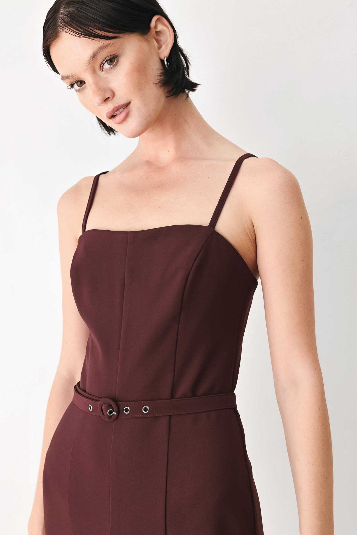 A woman modeling a dark burgundy wide-leg jumpsuit with thin spaghetti straps and a matching waist belt | FREEMARKET