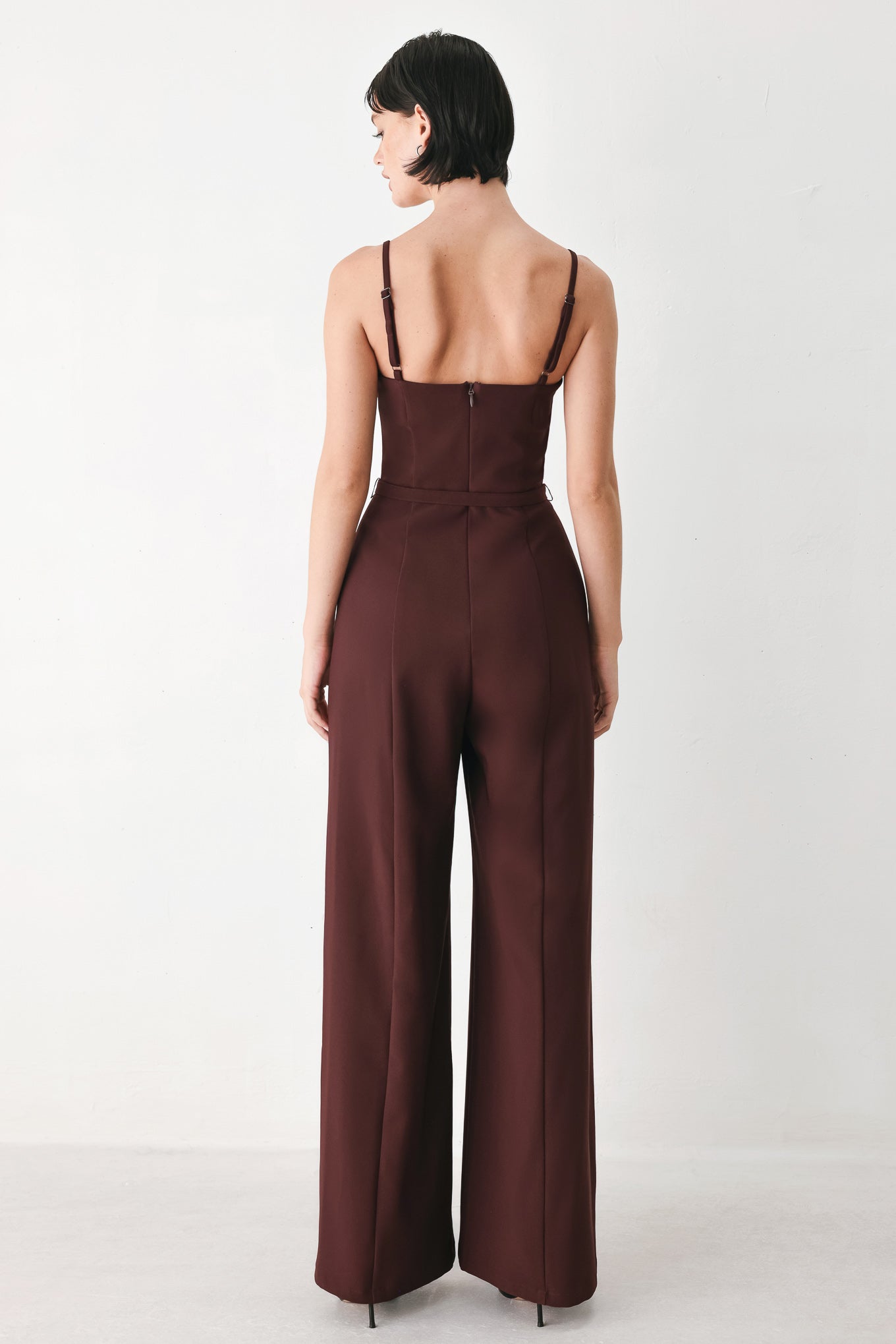 A woman modeling a dark burgundy wide-leg jumpsuit with thin spaghetti straps and a matching waist belt | FREEMARKET