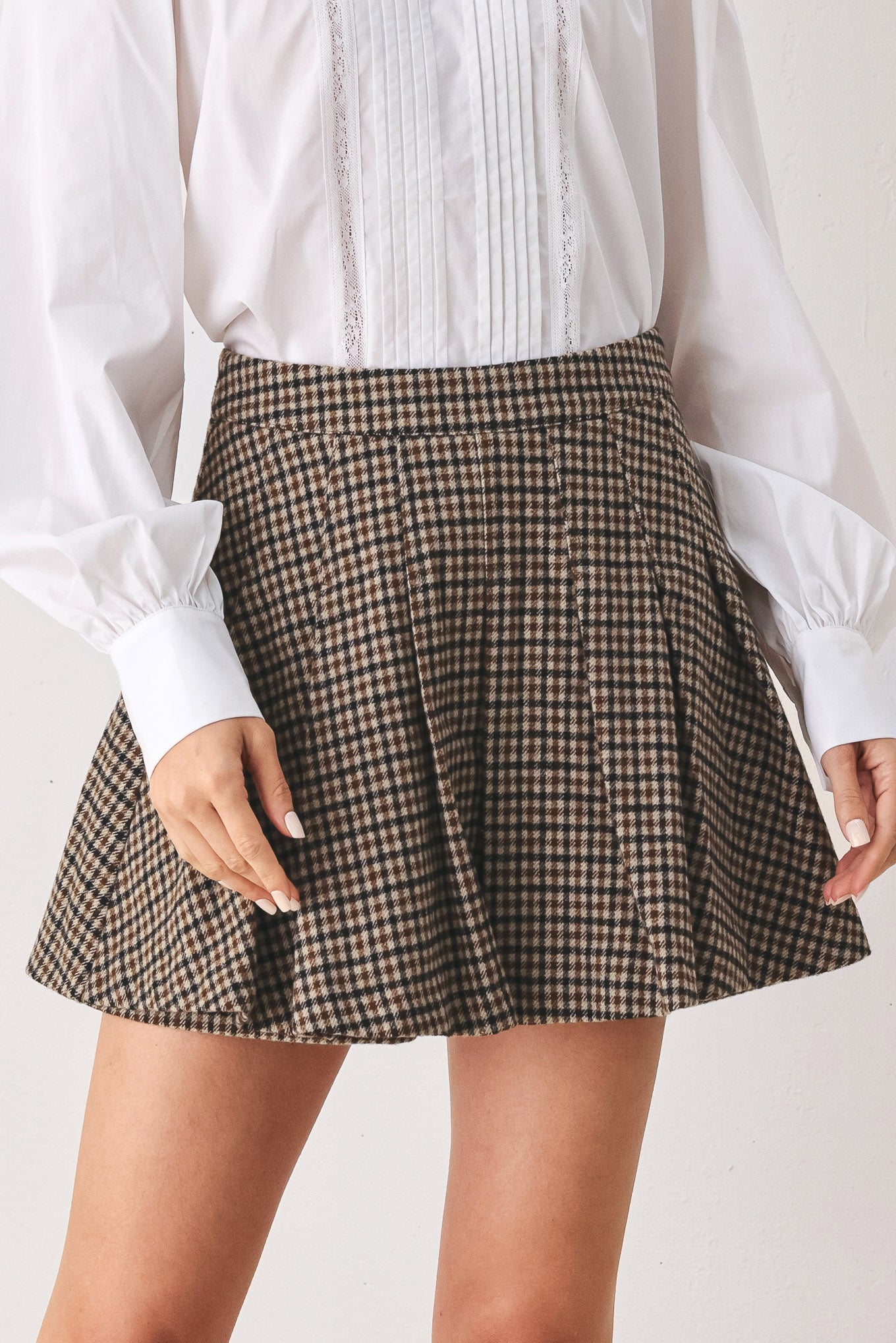 A close-up of a person wearing a brown and beige plaid pleated houndstooth mini skort | FREEMARKET