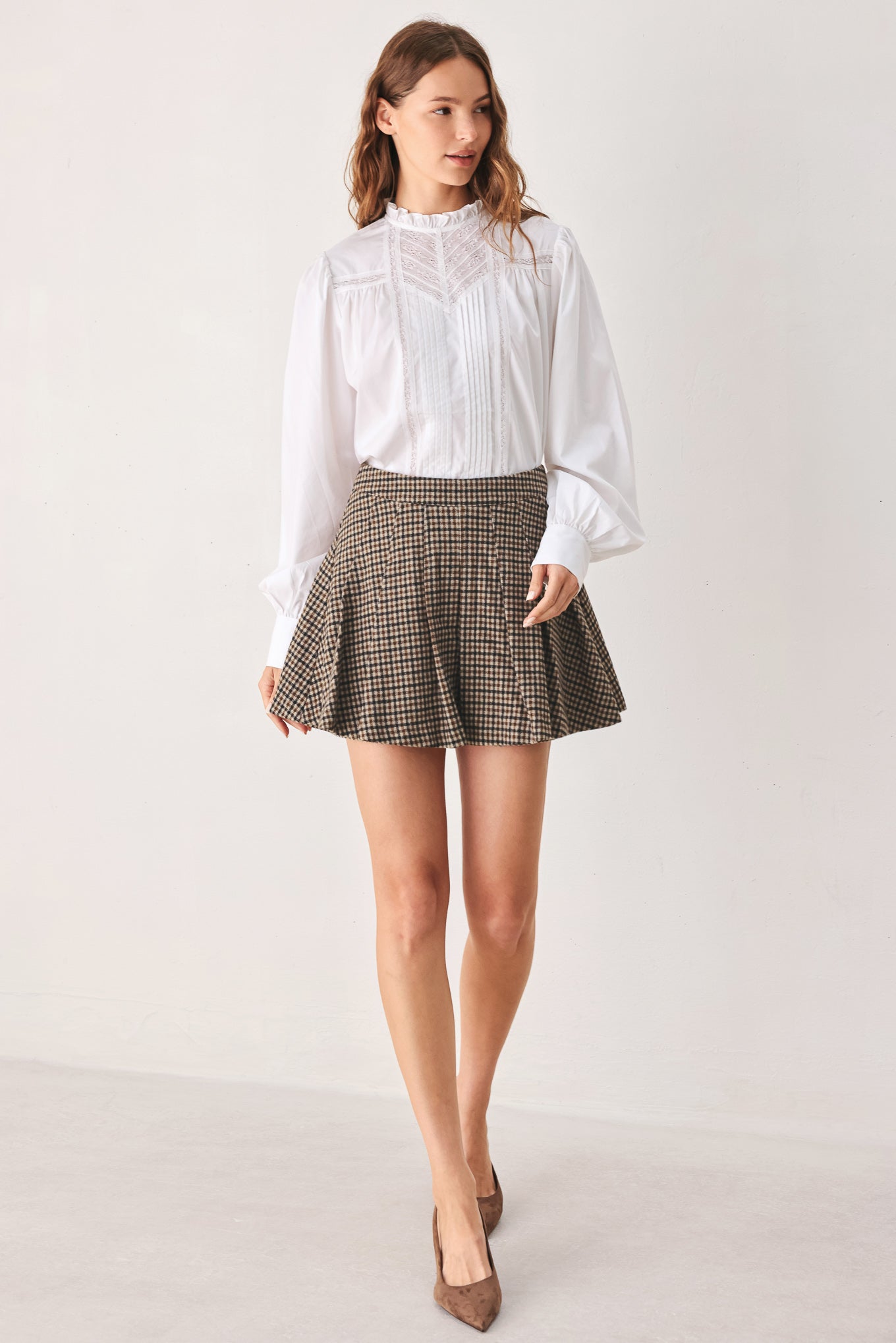 A close-up of a person wearing a brown and beige plaid pleated houndstooth mini skort | FREEMARKET