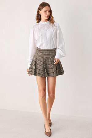 A close-up of a person wearing a brown and beige plaid pleated houndstooth mini skort | FREEMARKET
