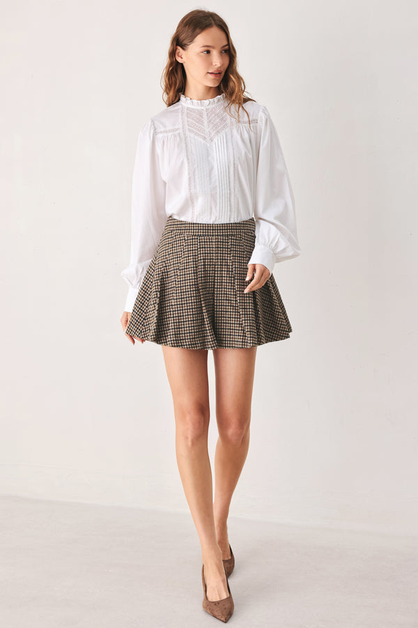 A close-up of a person wearing a brown and beige plaid pleated houndstooth mini skort | FREEMARKET