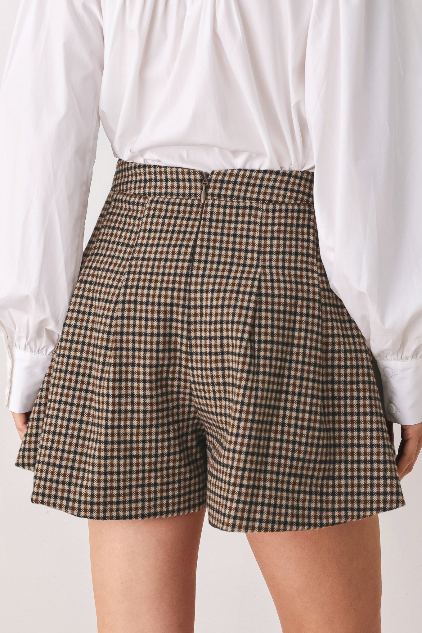 A close-up of a person wearing a brown and beige plaid pleated houndstooth mini skort | FREEMARKET