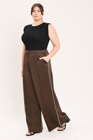 A woman modeling a black sleeveless ribbed top and high-waisted brown wide-leg pants with a thin white side stripe, standing against a plain light background.