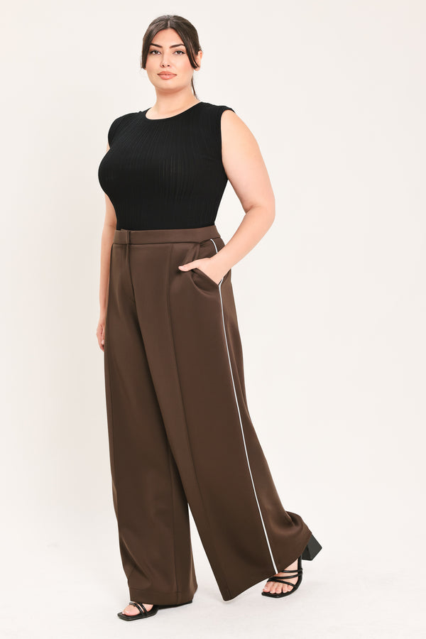 A woman modeling a black sleeveless ribbed top and high-waisted brown wide-leg pants with a thin white side stripe, standing against a plain light background.