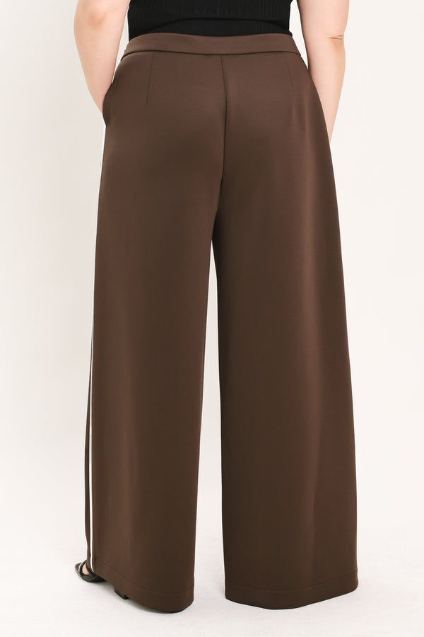 A person shown from the back wearing high-waisted, wide-leg brown pants with a black top, photographed against a plain light background.