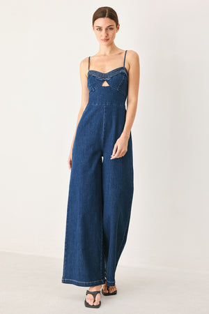 Woman wearing a blue denim jumpsuit featuring cami top with cut out, wide leg and back zipper closure | FREEMARKET