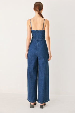 Woman wearing a blue denim jumpsuit featuring cami top with cut out, wide leg and back zipper closure | FREEMARKET