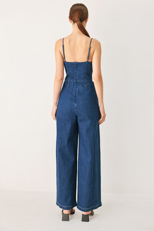 Woman wearing a blue denim jumpsuit featuring cami top with cut out, wide leg and back zipper closure | FREEMARKET