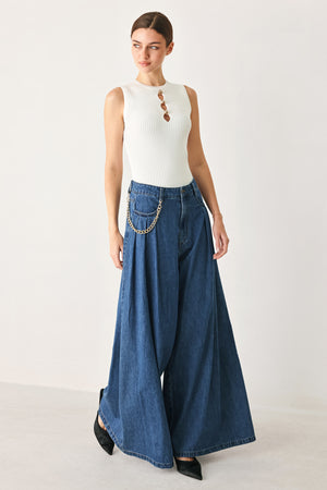 Woman wearing a pair of extra wide-leg blue denim jeans with front closure, pockets, pleats, and chain detail | FREEMARKET