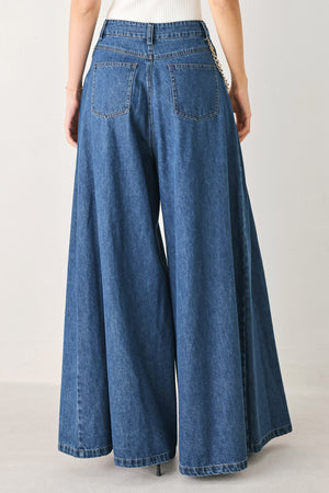 Woman wearing a pair of extra wide-leg blue denim jeans with front closure, pockets, pleats, and chain detail | FREEMARKET
