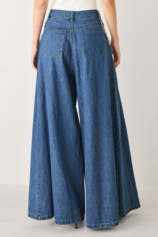 Woman wearing a pair of extra wide-leg blue denim jeans with front closure, pockets, pleats, and chain detail | FREEMARKET