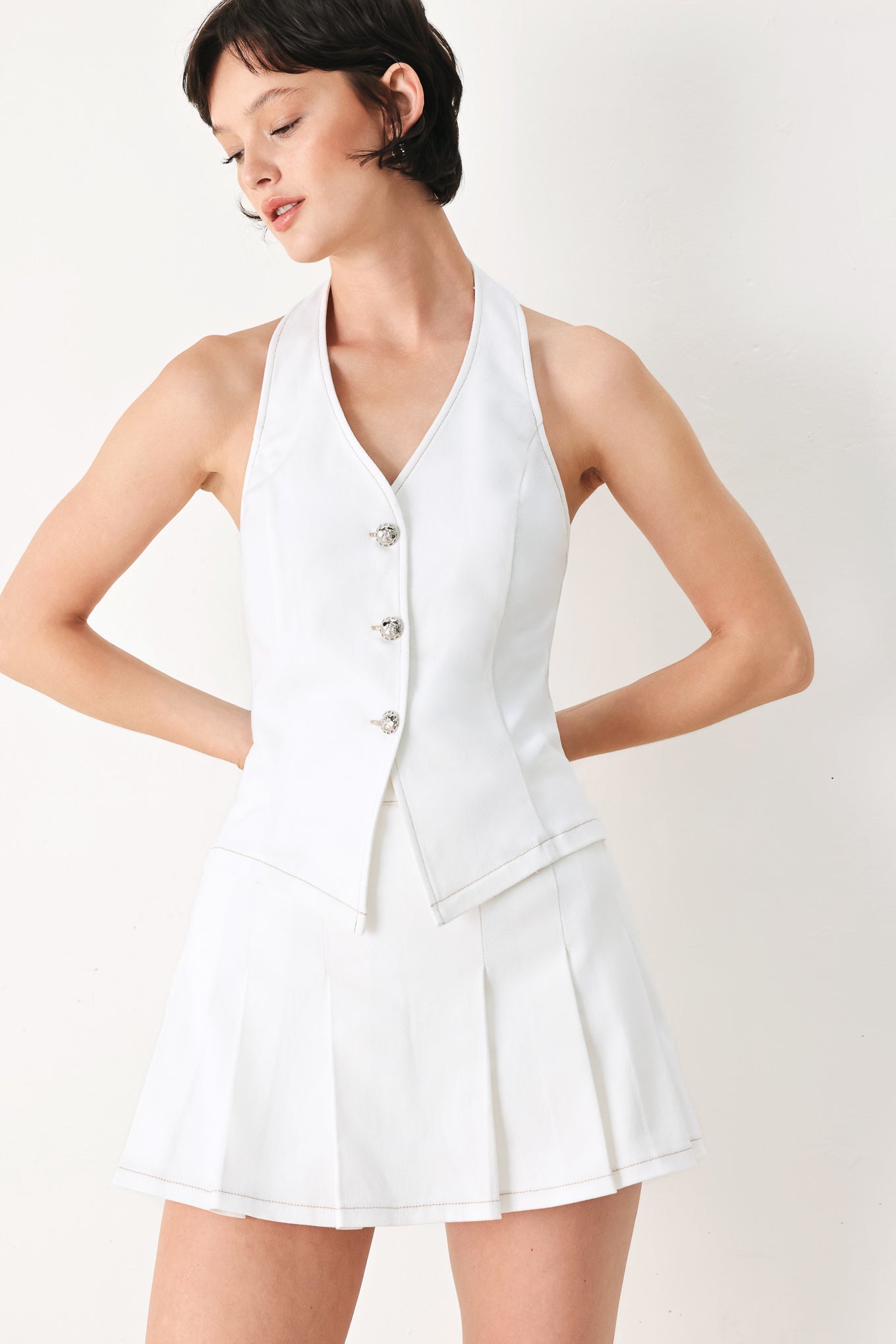 Woman wearing a white pleated skort with a button on each side of the waistband | FREEMARKET