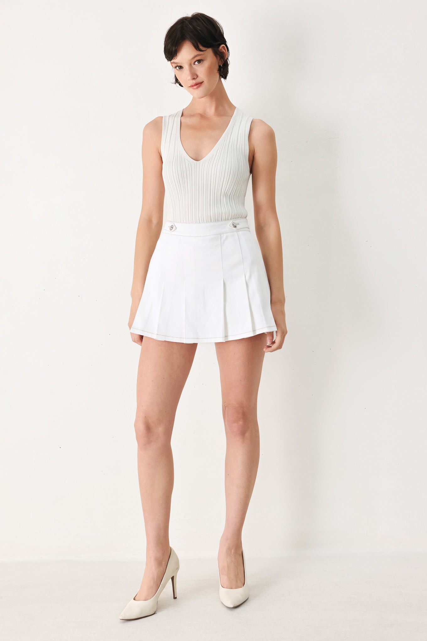 Woman wearing a white pleated skort with a button on each side of the waistband | FREEMARKET