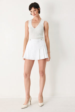 Woman wearing a white pleated skort with a button on each side of the waistband | FREEMARKET