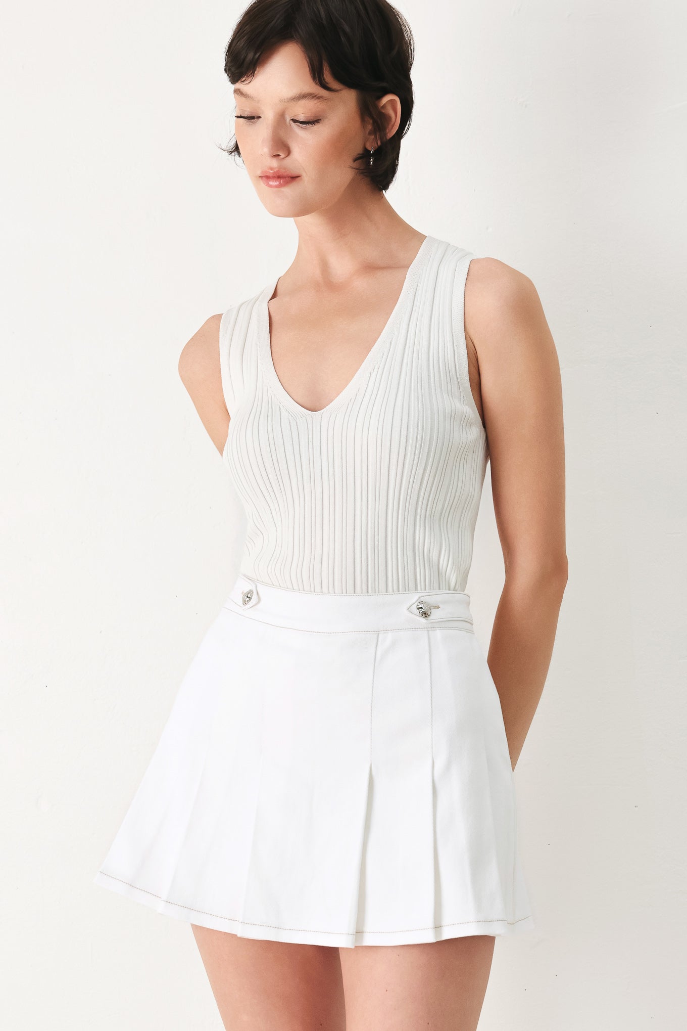 Woman wearing a white pleated skort with a button on each side of the waistband | FREEMARKET