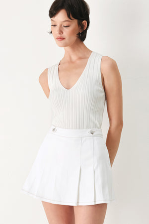 Woman wearing a white pleated skort with a button on each side of the waistband | FREEMARKET