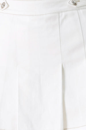Woman wearing a white pleated skort with a button on each side of the waistband | FREEMARKET