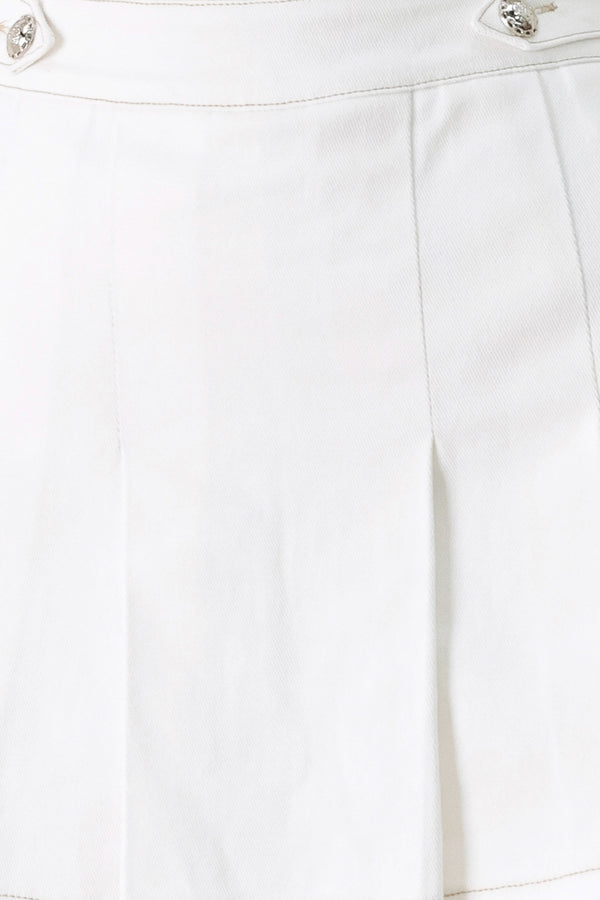 Woman wearing a white pleated skort with a button on each side of the waistband | FREEMARKET