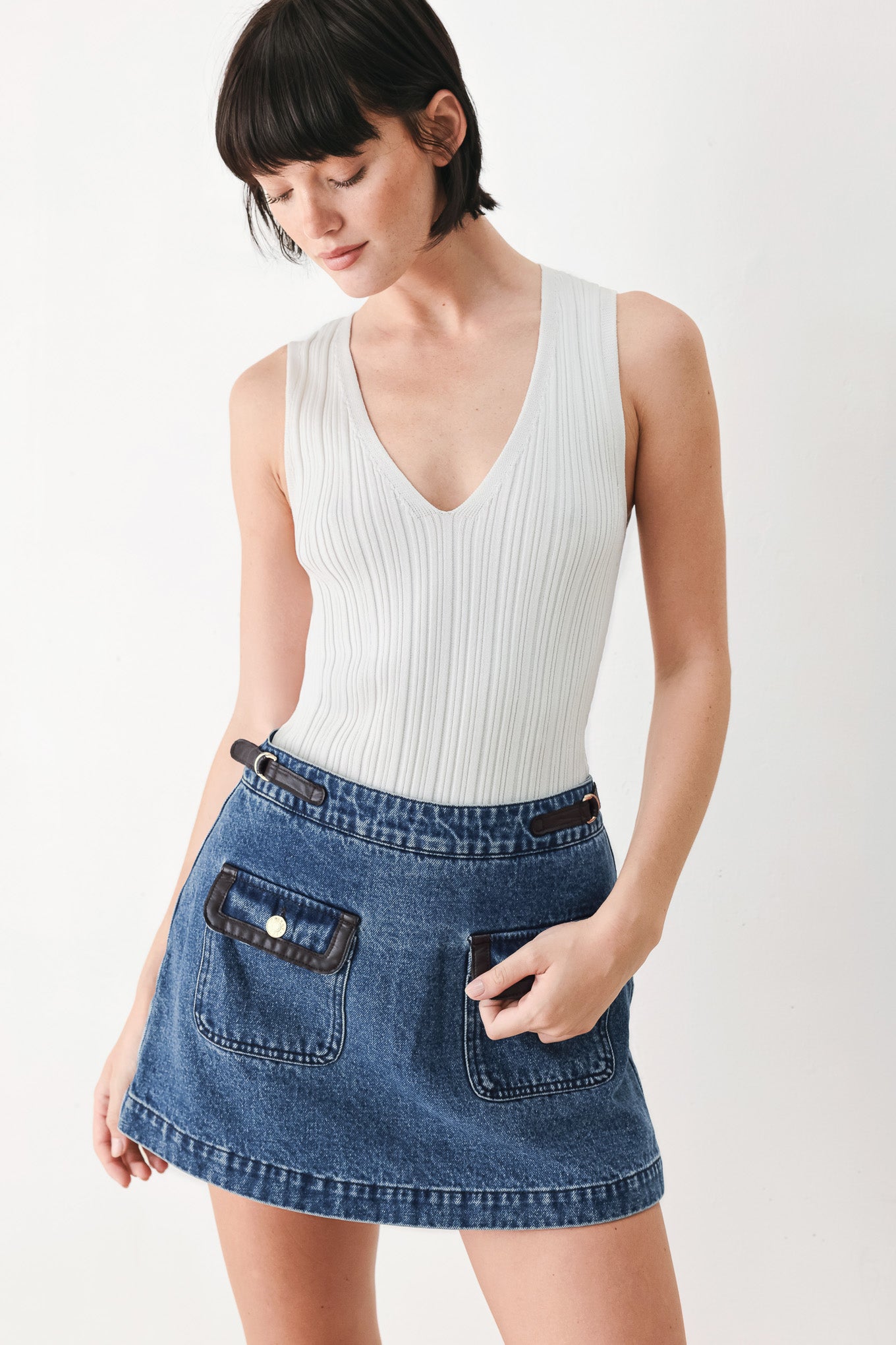 A model wearing a blue denim mini skort with dark brown leather accents on the waistband and pocket flaps | FREEMARKET