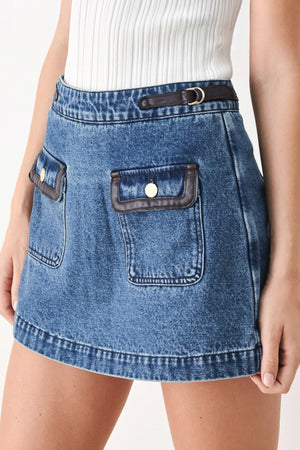 A model wearing a blue denim mini skort with dark brown leather accents on the waistband and pocket flaps | FREEMARKET