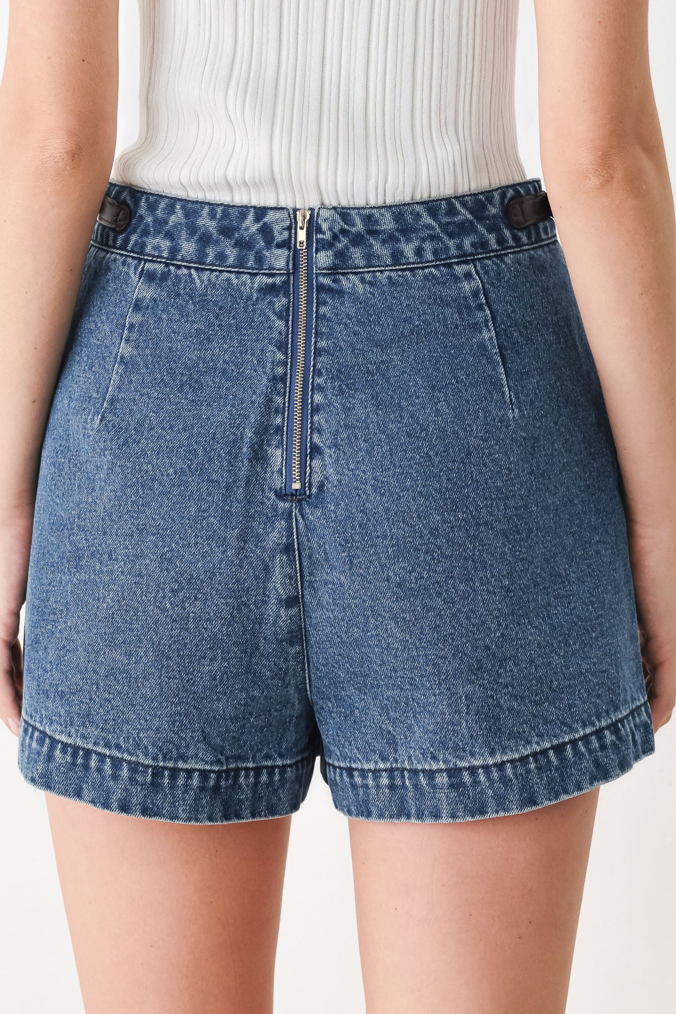 A model wearing a blue denim mini skort with dark brown leather accents on the waistband and pocket flaps | FREEMARKET