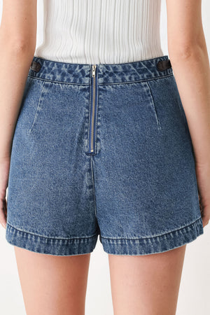 A model wearing a blue denim mini skort with dark brown leather accents on the waistband and pocket flaps | FREEMARKET